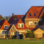 Row of traditional Dutch-style houses with orange gabled roofs under golden hour sunlight.