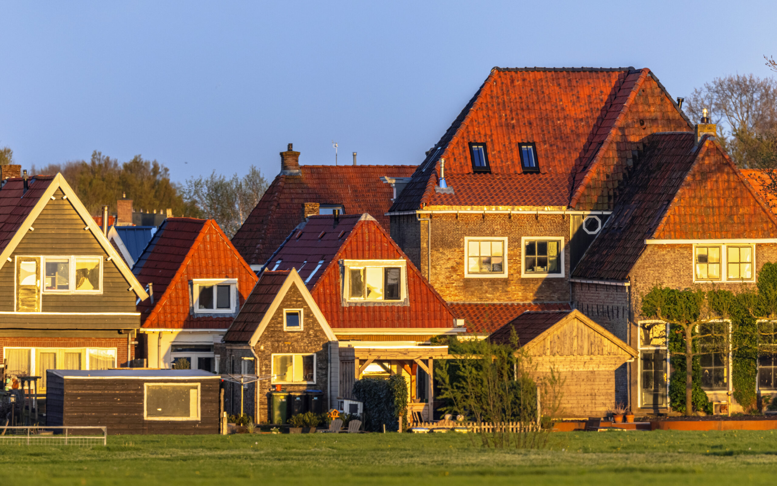 Row of traditional Dutch-style houses with orange gabled roofs under golden hour sunlight.