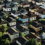 An aerial view of a densely packed residential neighborhood featuring colorful two-story houses with dark gabled roofs and tropical palm trees.