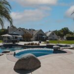 Luxury villa and backyard landscape design featuring a custom swimming pool with rock features and a water slide.