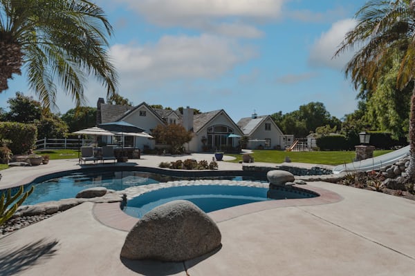 Luxury villa and backyard landscape design featuring a custom swimming pool with rock features and a water slide.